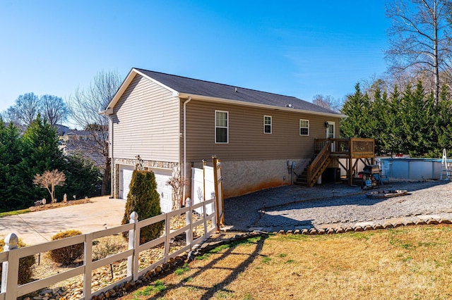 rear view of property featuring a garage, an outdoor pool, concrete driveway, stairs, and fence