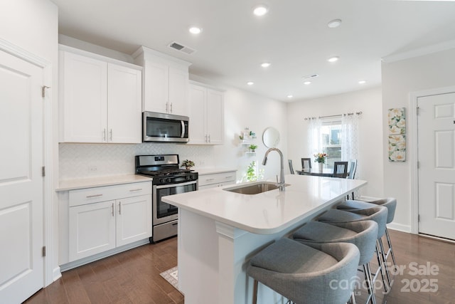 kitchen with dark wood-style floors, a center island with sink, a sink, stainless steel appliances, and a kitchen bar