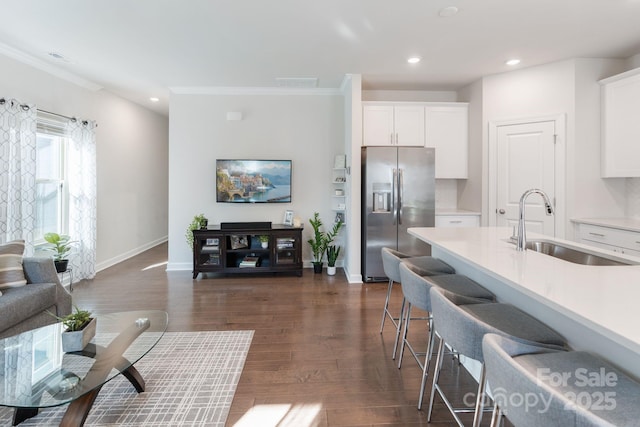 kitchen with dark wood-type flooring, stainless steel fridge with ice dispenser, a breakfast bar area, light countertops, and a sink