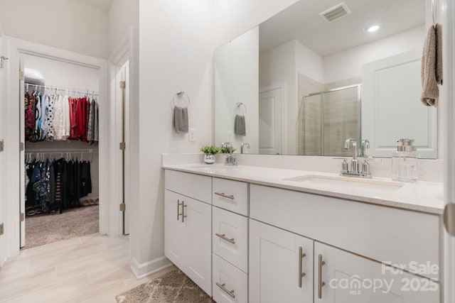 bathroom with a walk in closet, visible vents, a sink, a shower stall, and double vanity