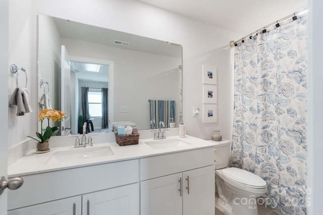 full bath with a sink, visible vents, toilet, and double vanity