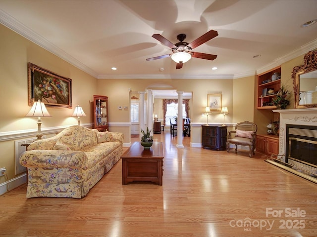 living room with light wood-type flooring, built in shelves, a glass covered fireplace, arched walkways, and ornate columns