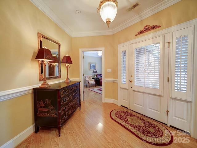 foyer featuring visible vents, ornamental molding, baseboards, and wood finished floors