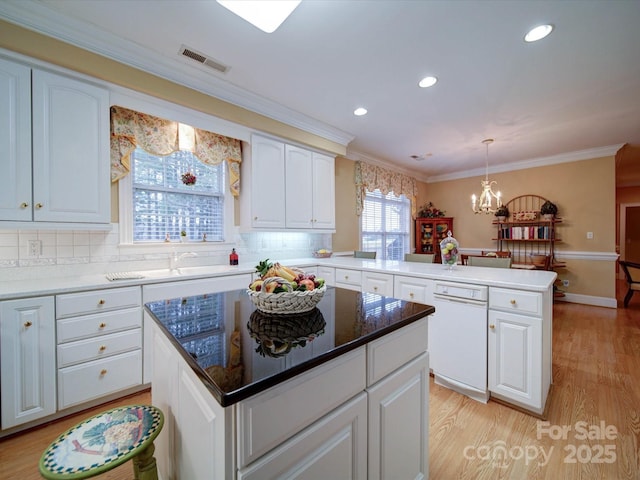 kitchen with visible vents, a sink, light wood-style floors, a peninsula, and white dishwasher