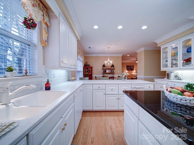 kitchen featuring dishwasher, light wood-type flooring, ornamental molding, a peninsula, and a sink