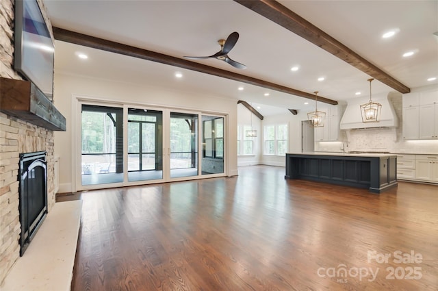 unfurnished living room featuring ceiling fan, wood finished floors, a fireplace, beam ceiling, and recessed lighting