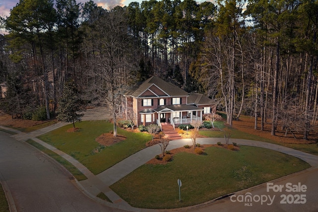 view of front of home featuring driveway, covered porch, and a front lawn