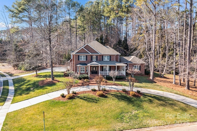 view of front of house with a forest view, covered porch, curved driveway, and a front yard