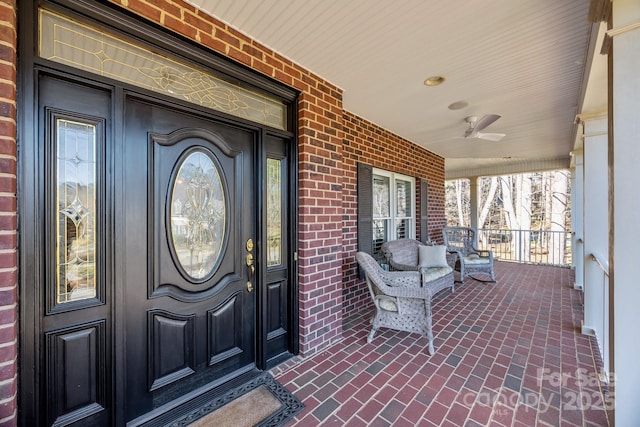 entrance to property with covered porch, a ceiling fan, and brick siding