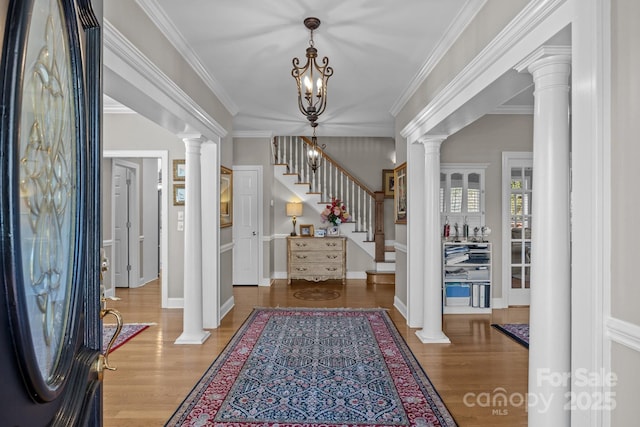 entryway with decorative columns, stairway, ornamental molding, wood finished floors, and baseboards