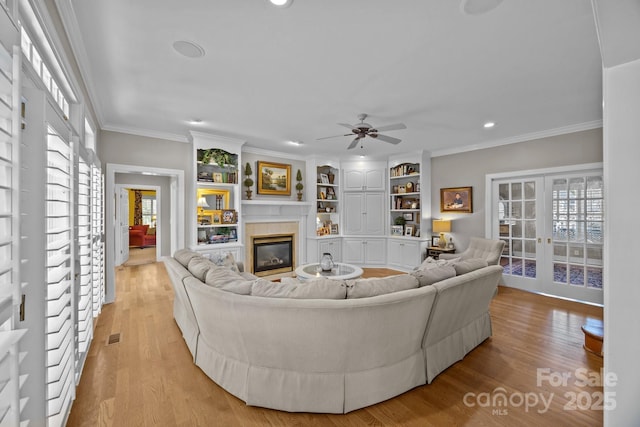 living room featuring french doors, light wood-type flooring, a glass covered fireplace, and crown molding