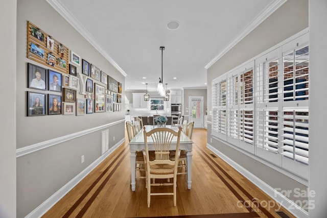 dining area with ornamental molding, recessed lighting, light wood-style flooring, and baseboards