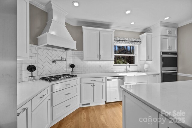 kitchen with white cabinetry, custom range hood, appliances with stainless steel finishes, and light countertops