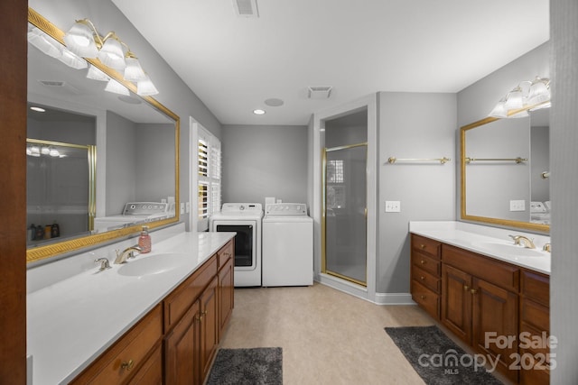 bathroom featuring a stall shower, two vanities, separate washer and dryer, and a sink