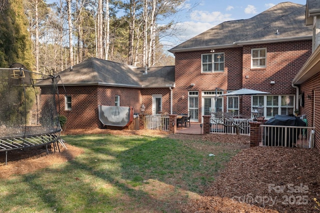 back of property featuring a trampoline, brick siding, a patio, a shingled roof, and a lawn