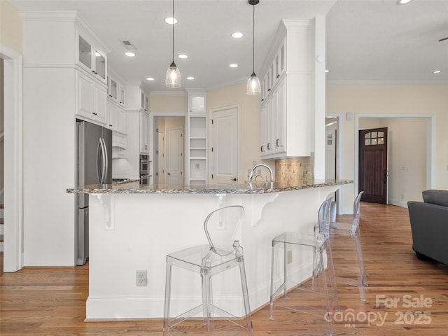 kitchen featuring stone counters, a peninsula, light wood-style floors, freestanding refrigerator, and glass insert cabinets