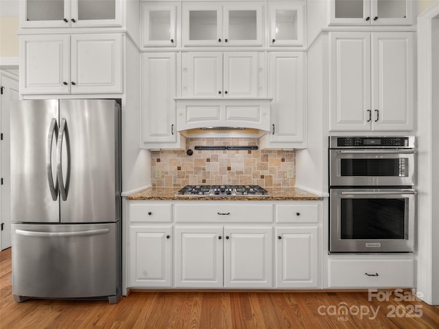 kitchen featuring appliances with stainless steel finishes, white cabinets, custom range hood, and light stone counters