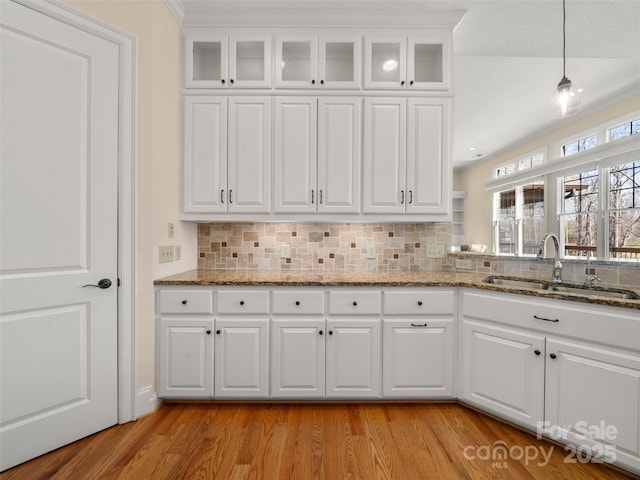 kitchen featuring white cabinetry, a sink, light wood-style flooring, and decorative backsplash