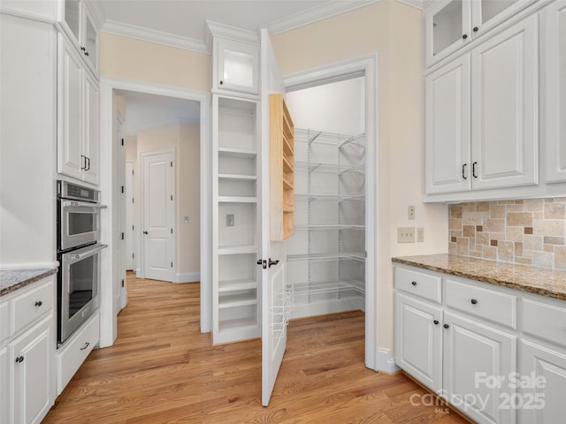 kitchen with light wood-style floors, stainless steel double oven, white cabinets, and crown molding