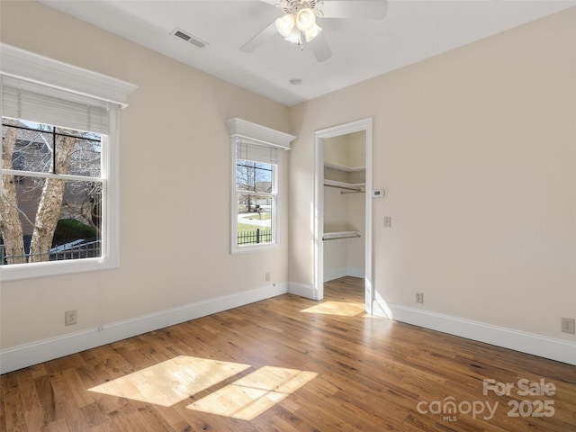 unfurnished bedroom with baseboards, visible vents, a ceiling fan, wood finished floors, and a spacious closet