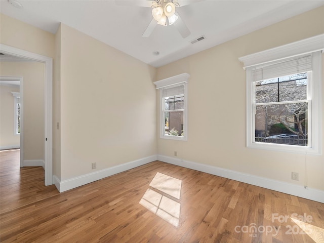 spare room with light wood-type flooring, plenty of natural light, visible vents, and baseboards