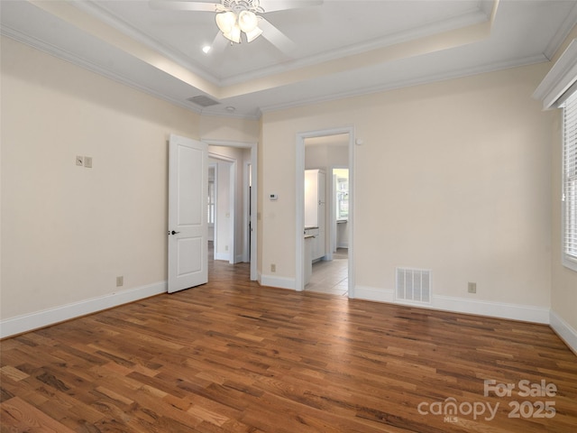 unfurnished room with baseboards, visible vents, a raised ceiling, wood finished floors, and crown molding