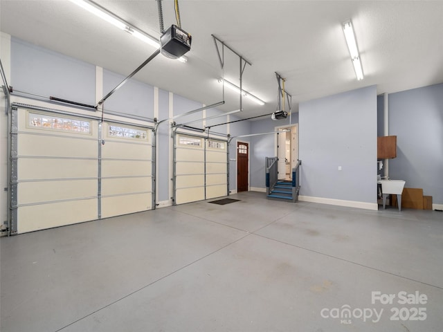 garage with a garage door opener, a sink, and baseboards