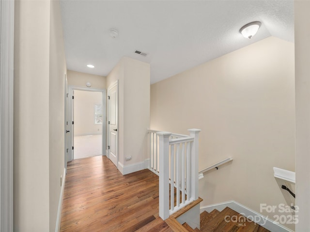 hallway featuring visible vents, vaulted ceiling, an upstairs landing, wood finished floors, and baseboards