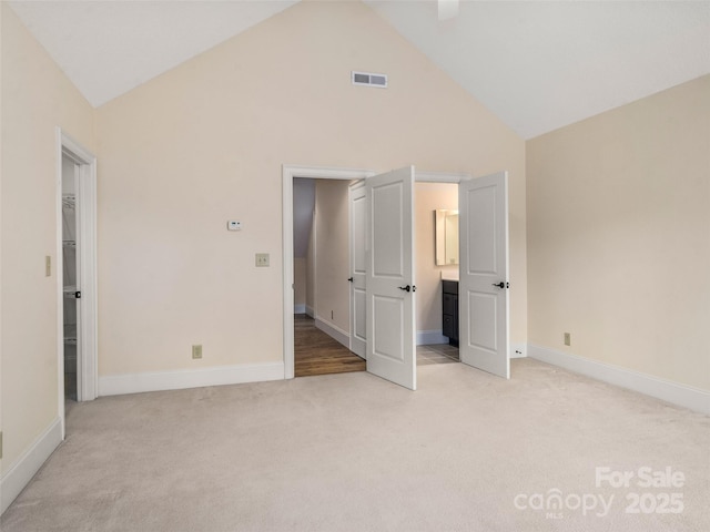 unfurnished bedroom with high vaulted ceiling, light colored carpet, visible vents, and baseboards