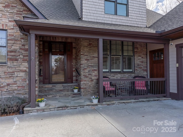 property entrance featuring a porch, stone siding, and roof with shingles