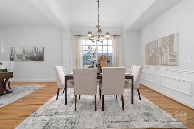 dining space with crown molding, a decorative wall, wainscoting, wood finished floors, and a chandelier