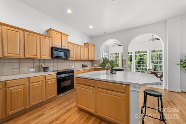 kitchen with tasteful backsplash, arched walkways, a breakfast bar area, light countertops, and black appliances