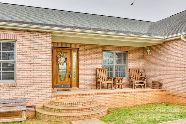 view of exterior entry with covered porch, brick siding, crawl space, and a shingled roof