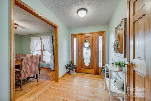 foyer entrance with light wood-style floors, a textured ceiling, and baseboards