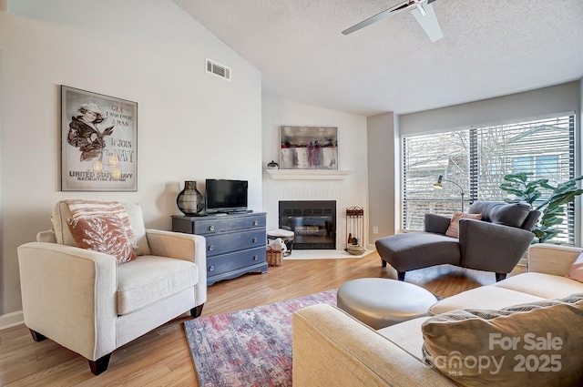 living room with visible vents, a fireplace with flush hearth, lofted ceiling, wood finished floors, and a textured ceiling