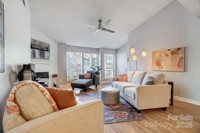 living room featuring wood finished floors, visible vents, a fireplace, ceiling fan, and vaulted ceiling