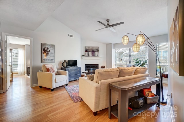 living area with a wealth of natural light, a fireplace, light wood-style floors, and vaulted ceiling