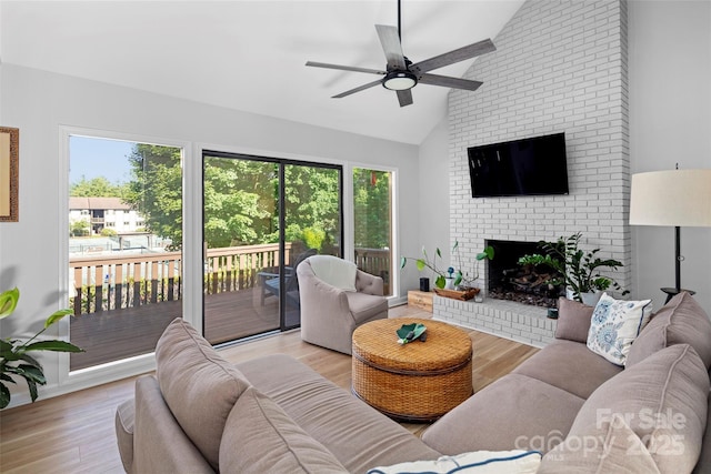 living area with a ceiling fan, lofted ceiling, a brick fireplace, and wood finished floors