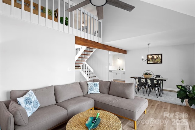 living area featuring baseboards, a high ceiling, stairs, ceiling fan with notable chandelier, and light wood-type flooring