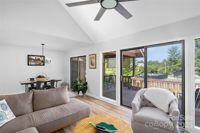 living room featuring light wood-style flooring, ceiling fan with notable chandelier, baseboards, and vaulted ceiling