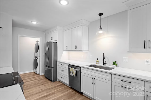 kitchen with light wood-style flooring, a sink, white cabinets, stacked washer and clothes dryer, and appliances with stainless steel finishes