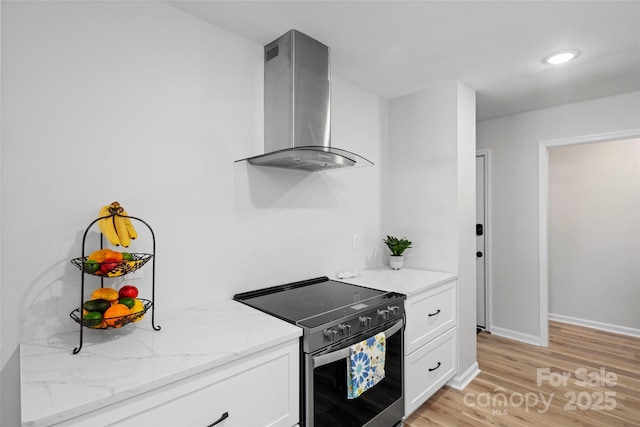 kitchen with stainless steel electric range oven, light stone countertops, white cabinets, light wood-style floors, and wall chimney exhaust hood