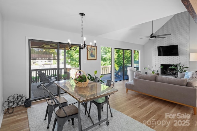 dining space featuring light wood finished floors, ceiling fan with notable chandelier, a brick fireplace, and lofted ceiling