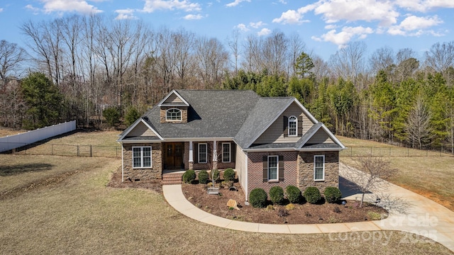 craftsman house featuring stone siding, concrete driveway, a front lawn, and fence