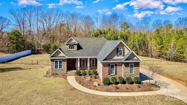 craftsman-style home featuring stone siding, driveway, a front lawn, and fence