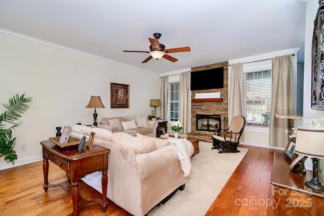 living room featuring baseboards, ceiling fan, a stone fireplace, hardwood / wood-style flooring, and crown molding