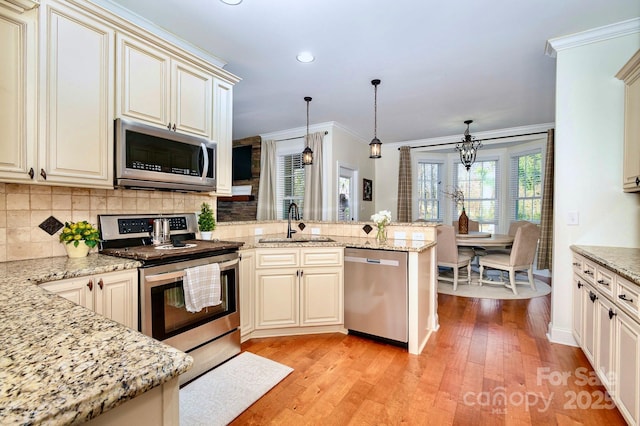 kitchen with tasteful backsplash, crown molding, appliances with stainless steel finishes, a peninsula, and a sink