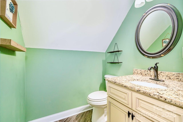 bathroom with toilet, lofted ceiling, wood finished floors, baseboards, and vanity