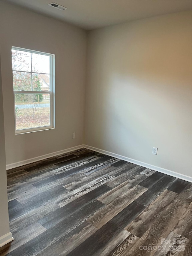 unfurnished room with dark wood finished floors, visible vents, and baseboards