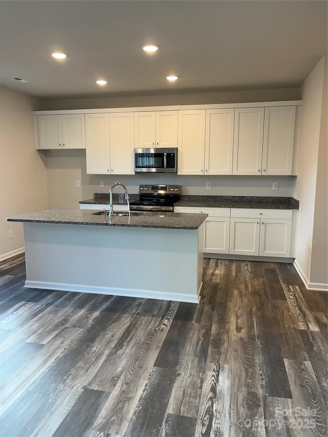 kitchen with dark wood-type flooring, dark stone countertops, white cabinets, stainless steel appliances, and a sink